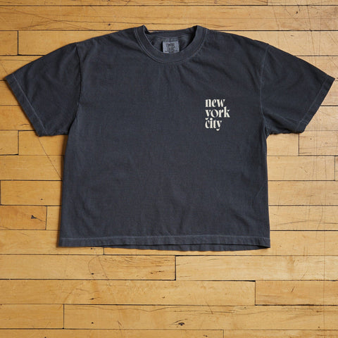 Black t-shirt with 'New York City' text on a wooden floor.