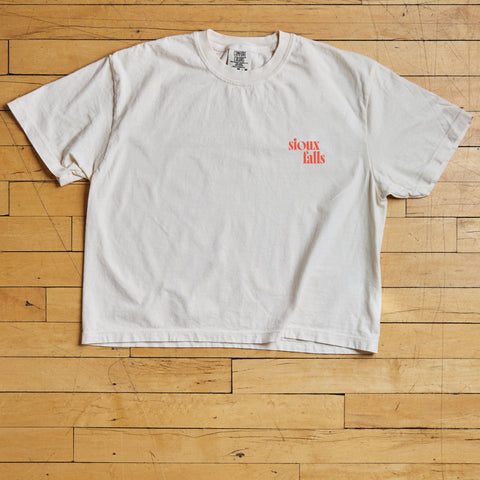 White t-shirt with 'Sioux Falls' text on a wooden floor