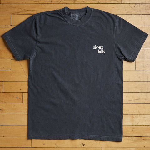 Black t-shirt with 'Sioux Falls' text on a wooden floor