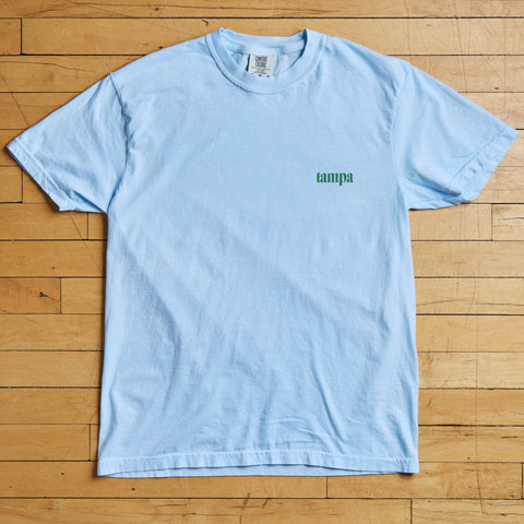 Light blue t-shirt with 'tampa' text on a wooden floor