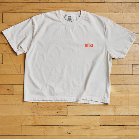 White t-shirt with a red Tulsa logo on a wooden floor