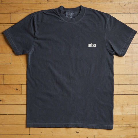 Black t-shirt with 'Tulsa' text on a wooden floor