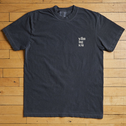 Black Wilmington t-shirt with white text on a wooden floor