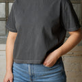 Person wearing a dark gray t-shirt and blue jeans against a textured wall.