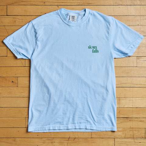 Light blue t-shirt with 'Sioux Falls' text on a wooden floor