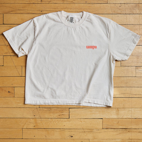White t-shirt with a red tampa logo on a wooden floor