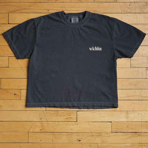 Black Wichita t-shirt with 'wichita' text on a wooden floor